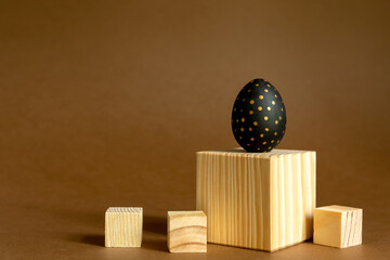 Trendy easter background. Golden and black painted eggs stand on wooden cubes, podiums on brown background.
