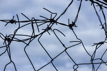 Metal barbed wire against an overcast blue sky in spring or winter and a hole in the fence. Protecting a parking lot, business or jail. 