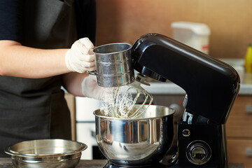 The pastry chef pours flour into the mixer bowl.