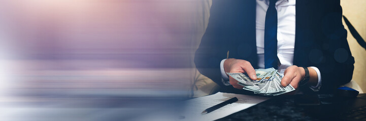 Businessman counting money, dollar banknotes at working desk. 
Panoramic financial  banner with copy space.