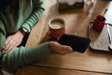 Obraz premium partial view of african american woman holding smartphone with blank screen near cup of cappuccino