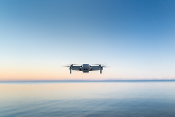 Fototapeta na wymiar A micro drone hovers in the air above a water horizon 
