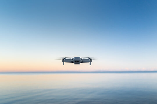 A micro drone hovers in the air above a water horizon 