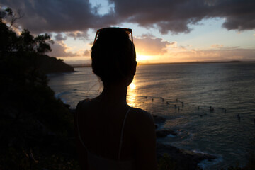 Silhouette of a woman watching surfers in the ocean during sunset