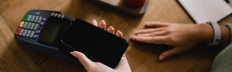 cropped view of african american woman paying with smartphone in cafe, banner