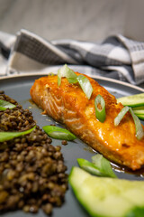Selective focus on a baked honey-soy glazed salmon fillet served with black beluga lentils with cucumber and green onions. Healthy fresh salmon steak for lunch or dinner. Side view