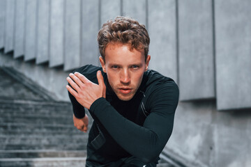 Runs forward. Young man in sportive clothes have workout outdoors at daytime