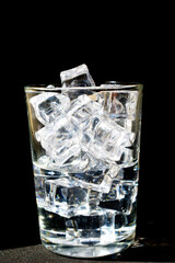 Transparent ice cubes are in a transparent glass on a black background.