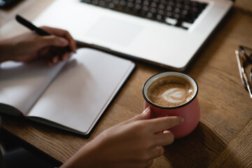 cropped view of african american woman holding cup with latte while writing in notebook