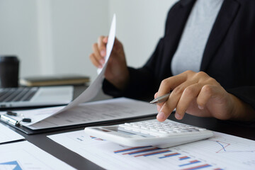 An Asian woman with a pen with one hand And the other side is looking at the bar graph document to...
