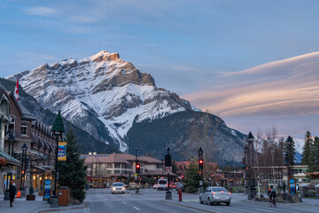 Street view of Banff Avenue in autumn evening. Snow capped Cascade Mountain with pink rosy sky in the background. Alberta, Canada. - obrazy, fototapety, plakaty