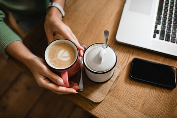 top view of african american woman holding cup of latte near sugar bowl in cafe