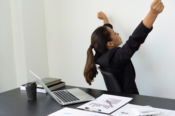 An Asian female finance worker in a suit sits at the office, resting, stretching, releasing and relieving fatigue during work.