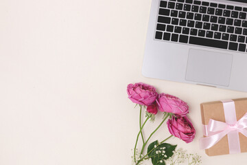 Bouquet of flowers, laptop and gift box with tied bow on a beige background. Online celebrate concept, present for Mothers Day with copyspace.