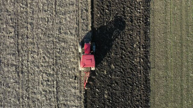 Aerial top view in dolly moving shot of tractor as plowing the ground on cultivated farm field, preparing soil for planting new crop next season.