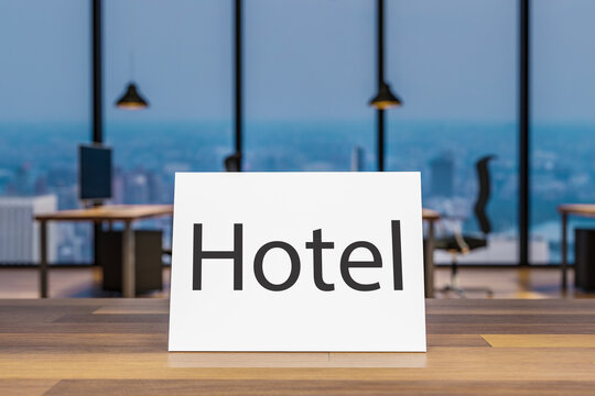Close up of wooden table with small paper sign hotel; blurry colorful modern interior background, 3D Illustration