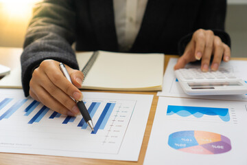 ..The hand of a female finance employee is using a pen to point at a graph on the desk in the office to explain the company's earnings at this morning's meeting.