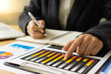 ..The hand of a female finance employee is using a pen to point at a graph on the desk in the office to explain the company's earnings at this morning's meeting.