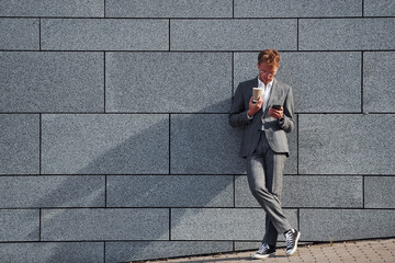 Against grey wall. Young businessman in grey formal wear is outdoors in the city