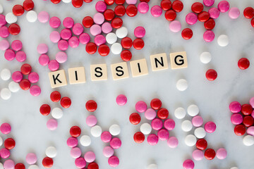 the words kissing written in scrabble tiles on a marble kitchen counter top surrounded by valentines candy