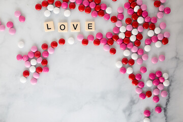 the word love written in scrabble tiles on a marble counter top surrounded by pink, red, and white chocolate candies