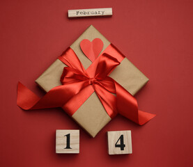 square box with red silk bow and wooden calendar with date 14 february on red background