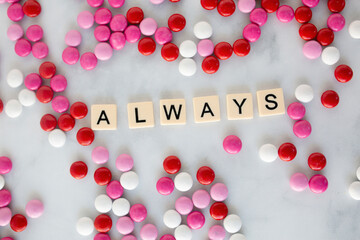 the word always written in scrabble tiles on a marble kitchen counter top surrounded by valentines candy