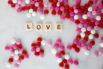 the word love written in scrabble tiles on a marble counter top surrounded by pink, red, and white chocolate candies