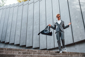 Going down by the stairs. Young businessman in grey formal wear is outdoors in the city