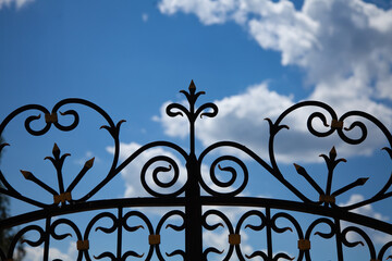 great photo. summer time. sunlight. photo from bottom to top. forging against the blue sky and white clouds. fragment of a forged fence close-up.