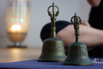 Closeup on Tibetan bells on yoga mat and legs of woman sitting in padmasana with lamp on background. Yogi in lotus pose doing meditation ritual ceremony in studio. Zen, spiritual concepts