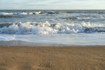 Sandy coast with waves, foam and blue sky