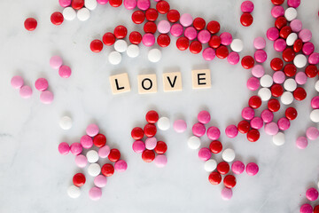 the word love written in scrabble tiles on a marble counter top surrounded by pink, red, and white chocolate candies