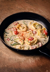 Ravioli in the white sauce with vegetables in pan on the wooden table.