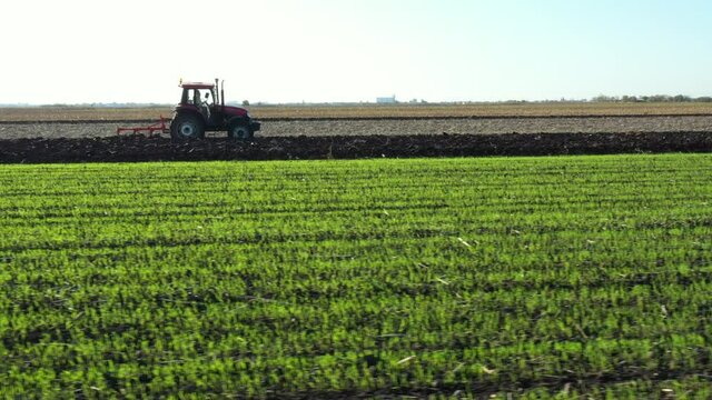 Dolly moving shot as parallel follow tractor is plowing the ground on cultivated farm field, preparing soil for planting new crop next season.
