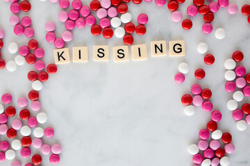 the words kissing written in scrabble tiles on a marble kitchen counter top surrounded by valentines candy