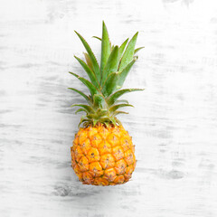 Pineapple white background. Ripe baby pineapple on a white wooden background. Tropical fruits. Top view. Free space for text.