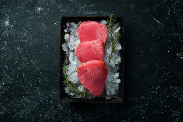 Raw tuna steak with spices on ice. On a dark background. Top view.