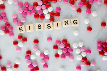 the words kissing written in scrabble tiles on a marble kitchen counter top surrounded by valentines candy