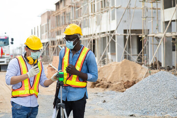 African american foreman and Asian man worker in safety hard hat helmet working together on construction site. wearing surgical face mask during coronavirus covid and flu outbreak