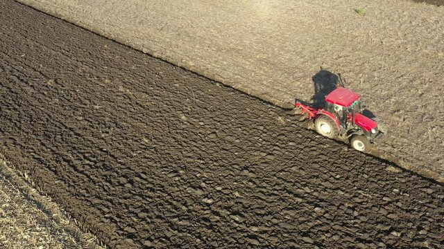 Aerial top view in dolly moving shot of tractor as plowing the ground on cultivated farm field, preparing soil for planting new crop next season.