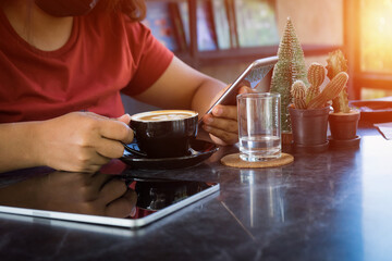 Young woman sitting in coffee shop at table,Female holding phone and looking on his screen in coffee shop. drinking coffee and using smartphone working with a tablet,The concept of the business idea.