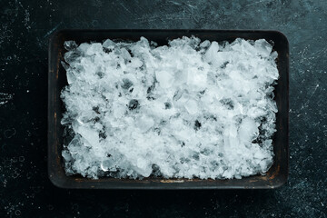 Crushed ice in a metal bowl on a black stone background. Top view. Free space for your text.