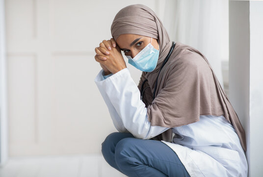 Pensive muslim woman doctor sitting next to wall in hospital