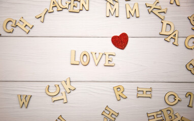 The word love made from decorative wooden letters on a light wooden background with glitter red hearts. Valentine's day poster, greeting card, banner
