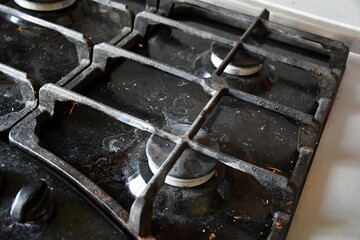 A dirty, stained and dusty black gas stove hob with cast-iron grilles.