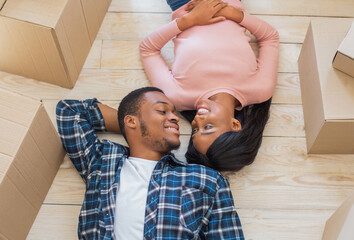 Above view of young black guy and his girlfriend lying on floor among carton boxes, looking at each...