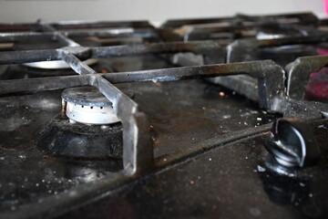 A dirty, stained and dusty black gas stove hob with cast-iron grilles.