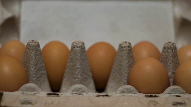 Close up of paper box with fresh organic eggs on a kitchen table. Concept. Baker female hand taking two egga from container for cooking.