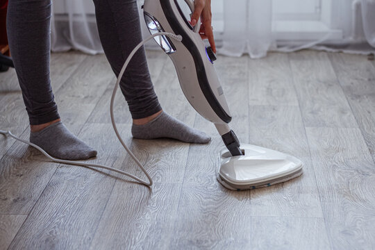 A young woman washes the floor with a modern steam cleaner.